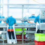 Workers wearing protective clothing and masks work in a food processing plant. Hygiene, quality control, manufacturing, and industrial production concept.