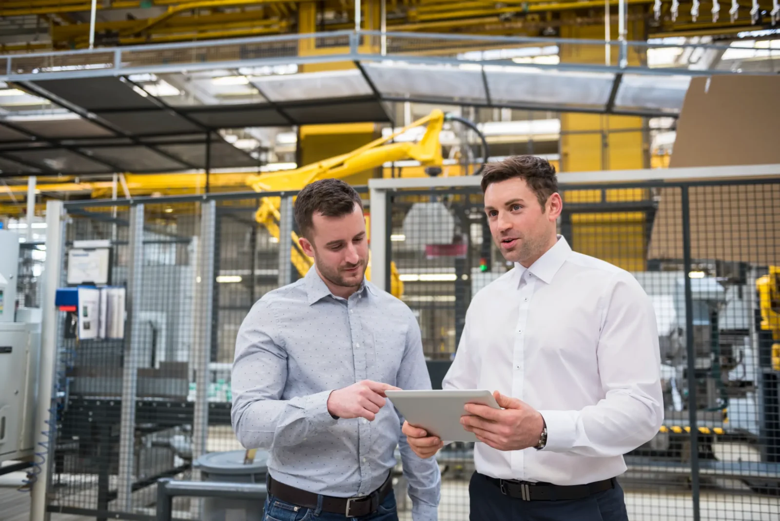 Two men discuss shop floor tracking data on a tablet in a factory.