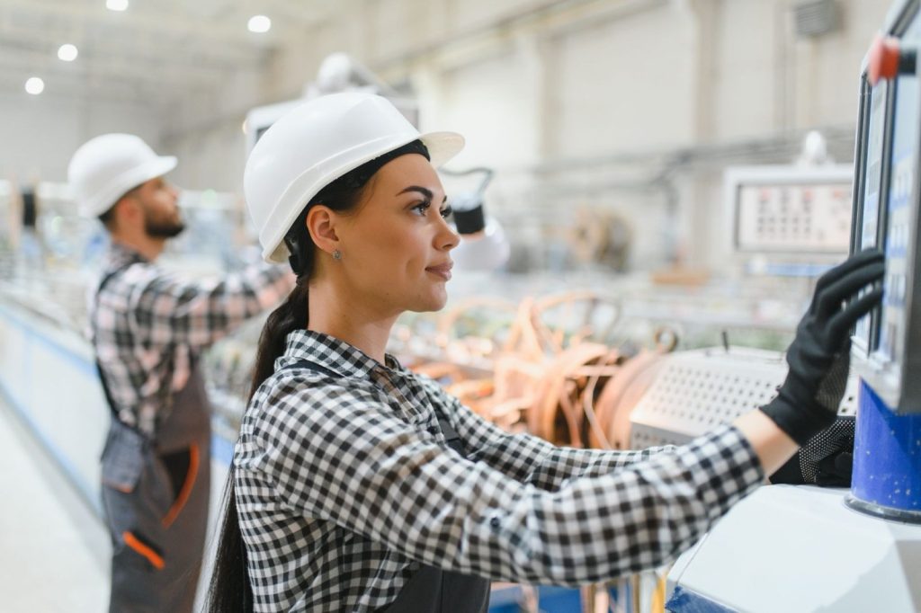 Factory worker in checkered shirt operating machinery, another in background