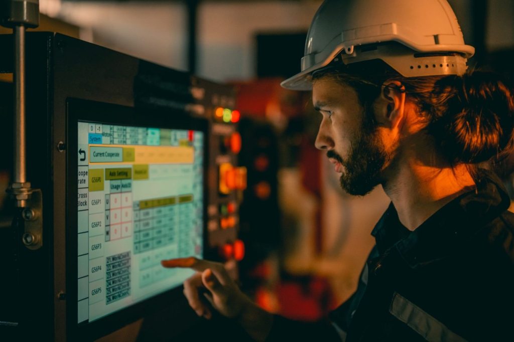 Engineer in hard hat uses touchscreen interface on industrial machinery.