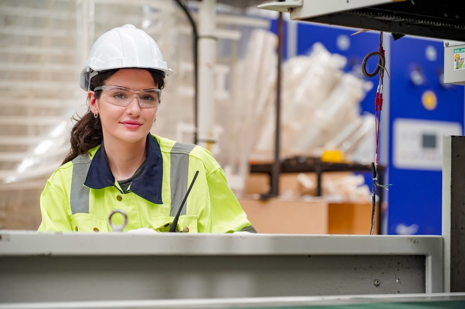 Woman in reflective safety jacket and hardhat working in factory