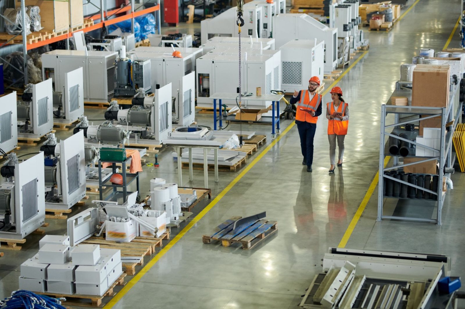 Two workers in safety vests discussing in a large warehouse with equipment