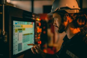 Engineer in hard hat uses touchscreen interface on industrial machinery.