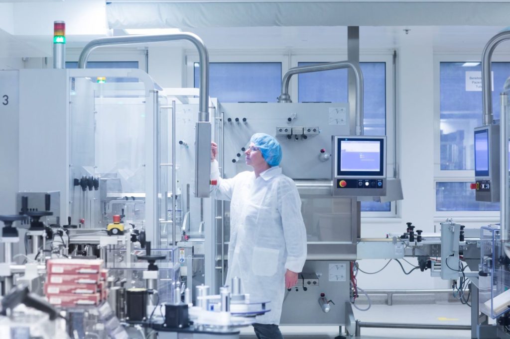 Technician in white lab coat working in a modern pharmaceutical manufacturing plant
